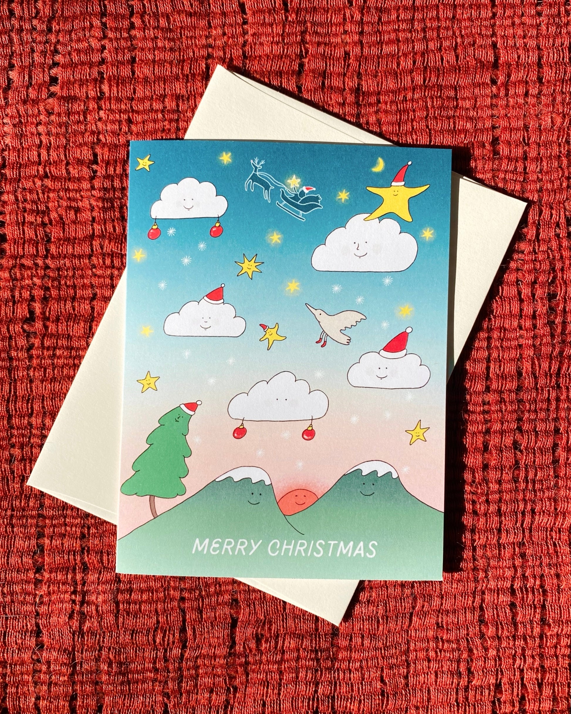 Cute Christmas Card with clouds with faces floating in the gradient sky along with stars, snow flakes above the mountains