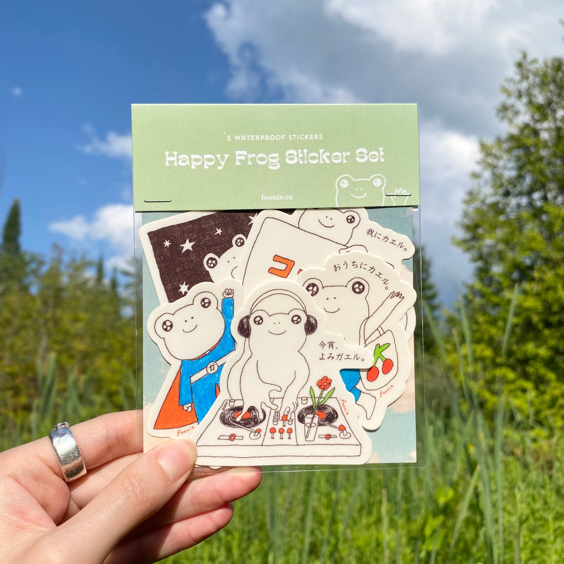 Pack of 'Happy Frog Sticker Set' held in front of a natural background with trees and blue sky