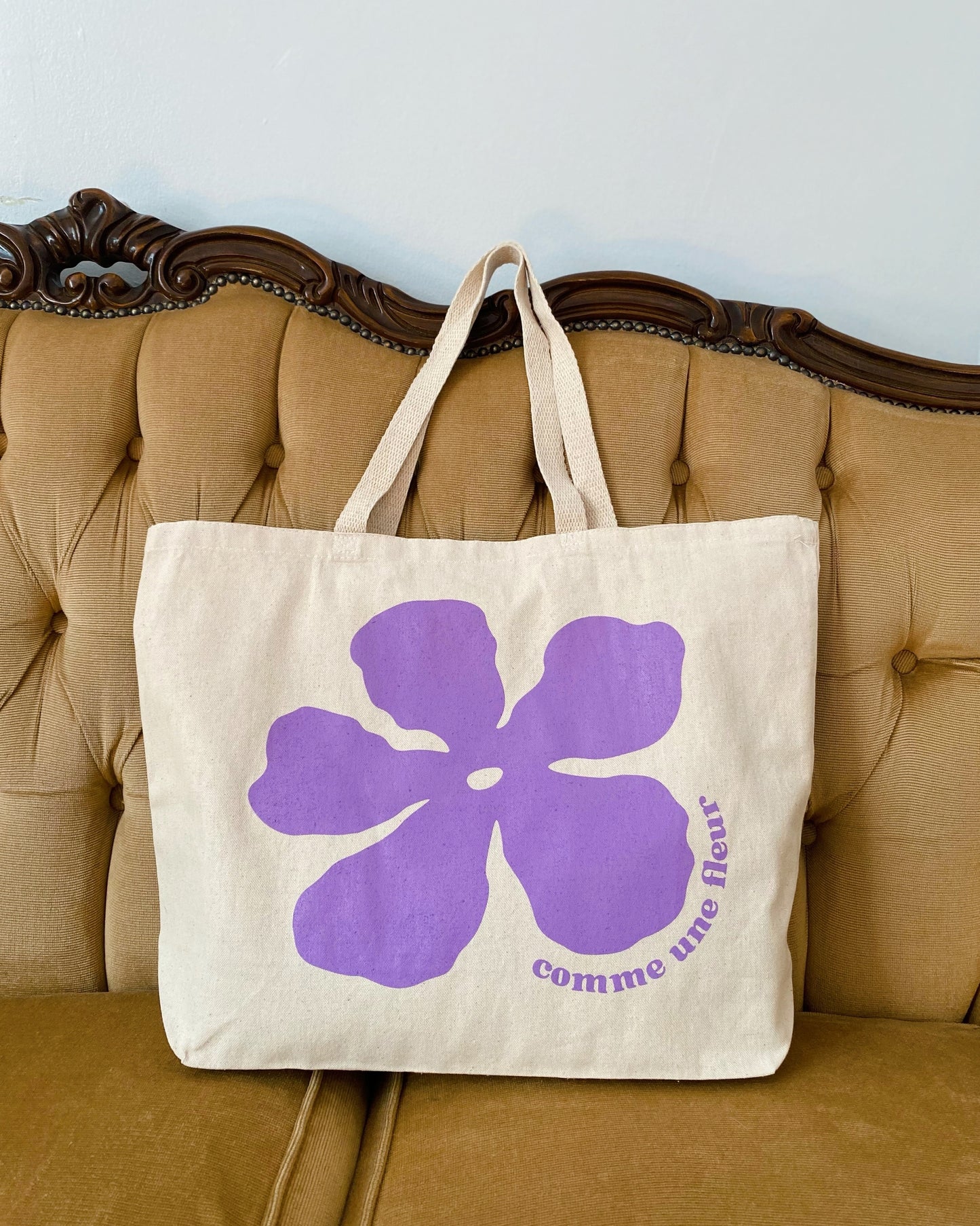 a heavy cotton tote bag with the large illustration of a purple flower on a vintage couch