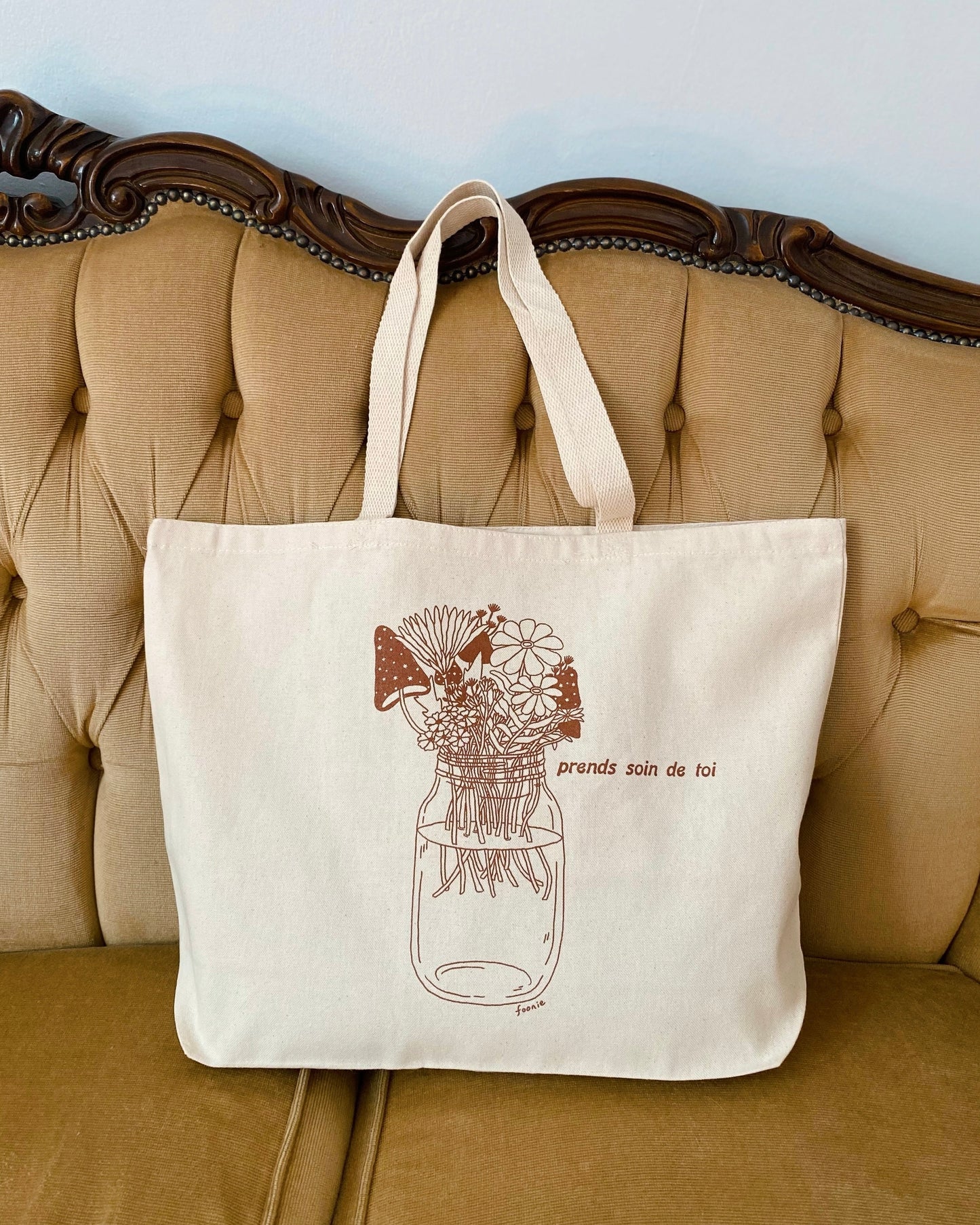 a heavy cotton tote bag with the illustration of flowers and mushrooms in a mason jar on a vintage couch
