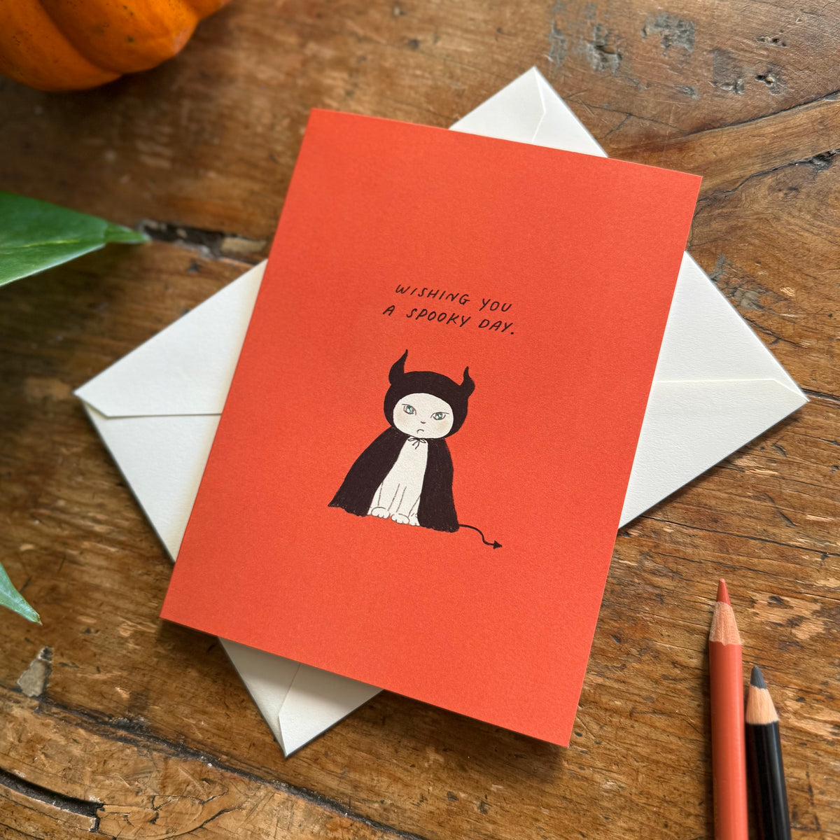 A halloween themed greeting card with the illustration of a cute cat wearing a divil costume.