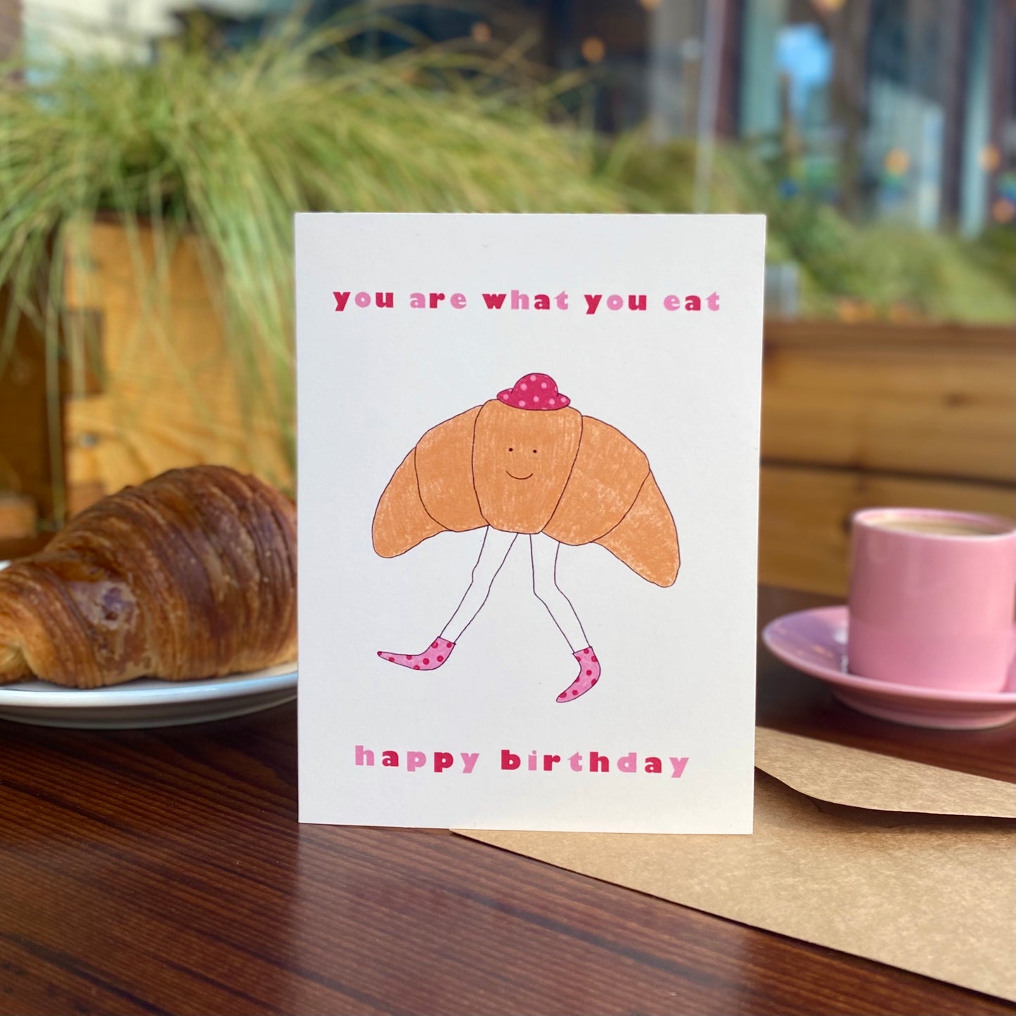 Silly and Cheeky Birthday Card with a cute croissant wearing pink socks and a red hat walking