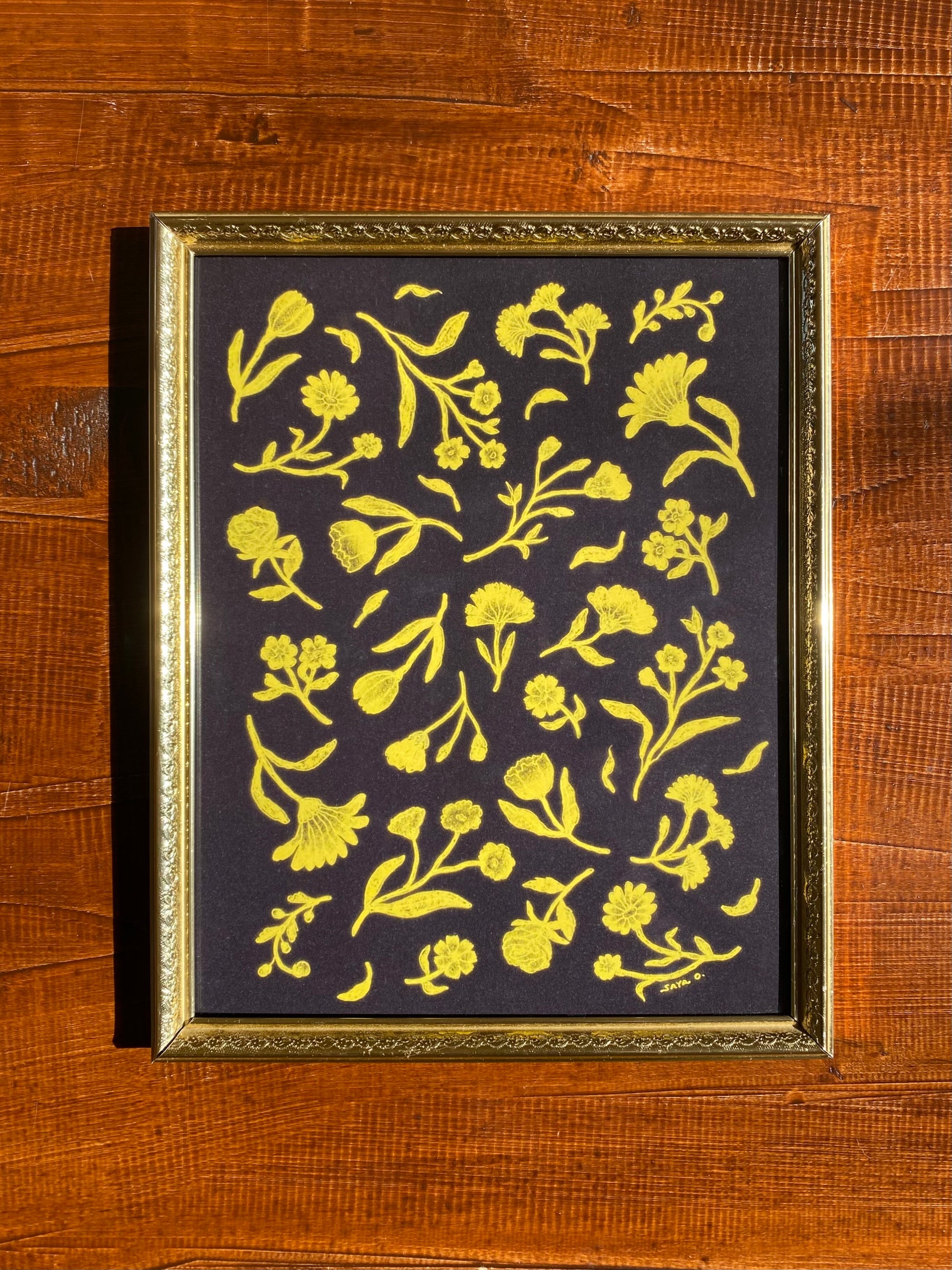 A classic floral print with deep yellow flowers on a black background in a gold frame